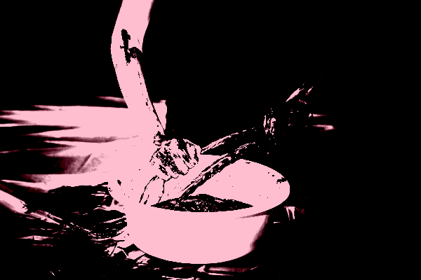 This image depicts hands covered in black mud wringing drenched feathers over a white bucket on a plastic tarp. The outline of a body dressed in black blends into the background.