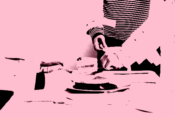 This image depicts outstretched arms, bound by canvas sleeves and straps, holding plates and waiting to receive a piece of a red and orange cake being served by another set of arms which are restricted in the same way.